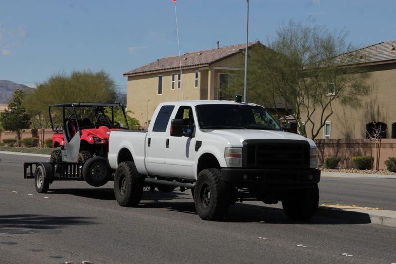 Lifted white Ford F-250 towing a side-by-side on a trailer